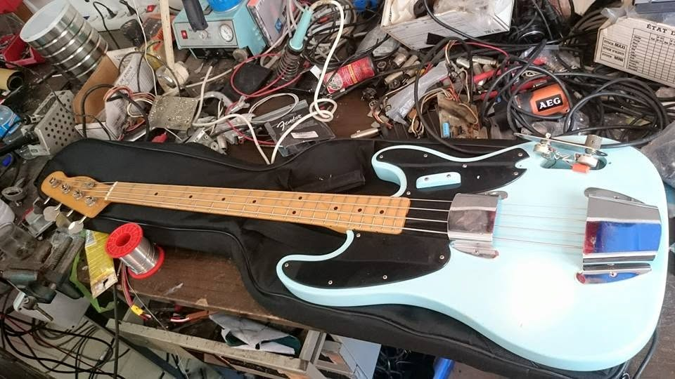 Pale blue electric bass lying across a crowded repair workbench